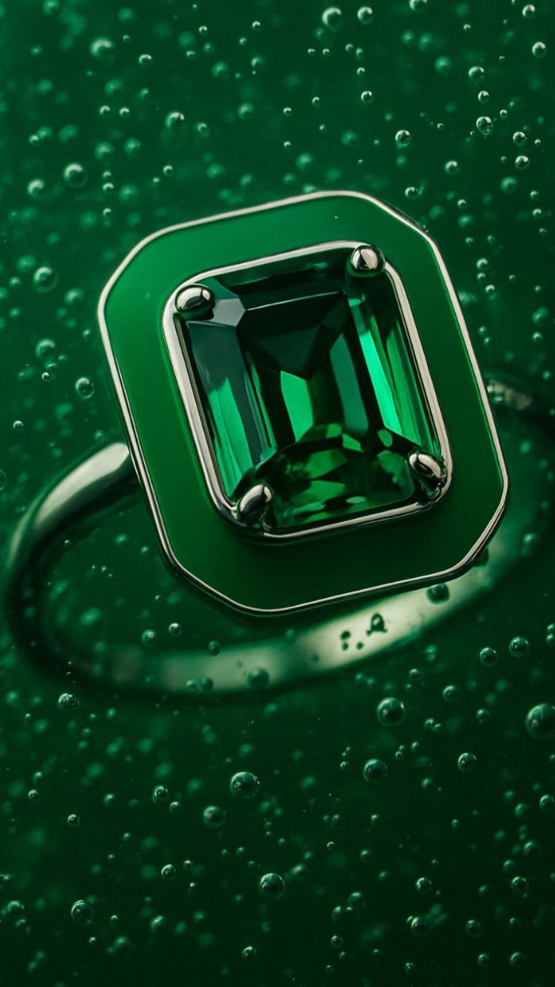 Underwater scene. A luxurious emerald ring slowly sinks deeper into rich green liquid. Tiny air b...
