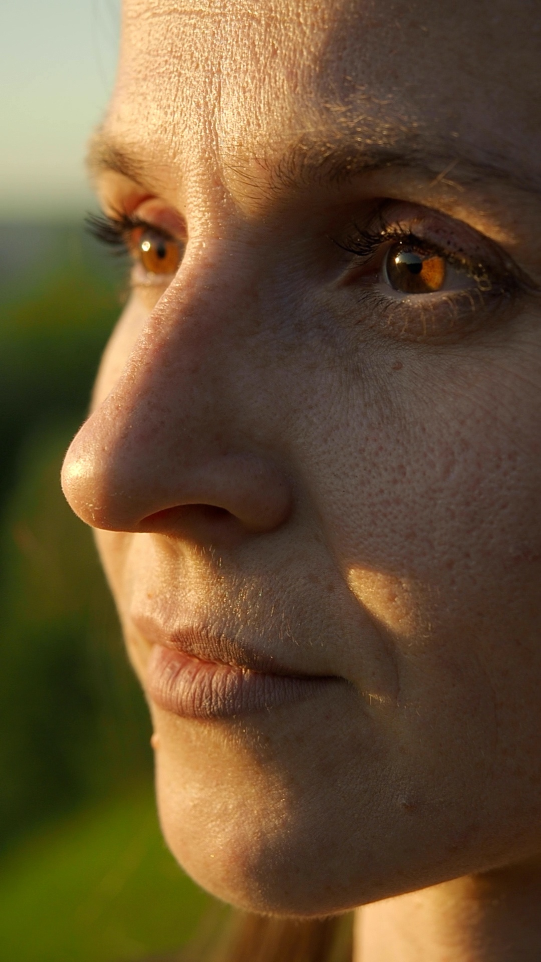Extreme macro close-up of a woman's face in warm golden hour sunlight. She remains completely sti...