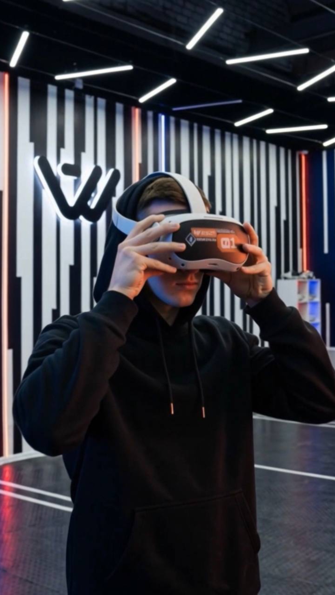 A young man in a striped VR room puts on a white '01' VR headset. As orange energy emanates, his ...