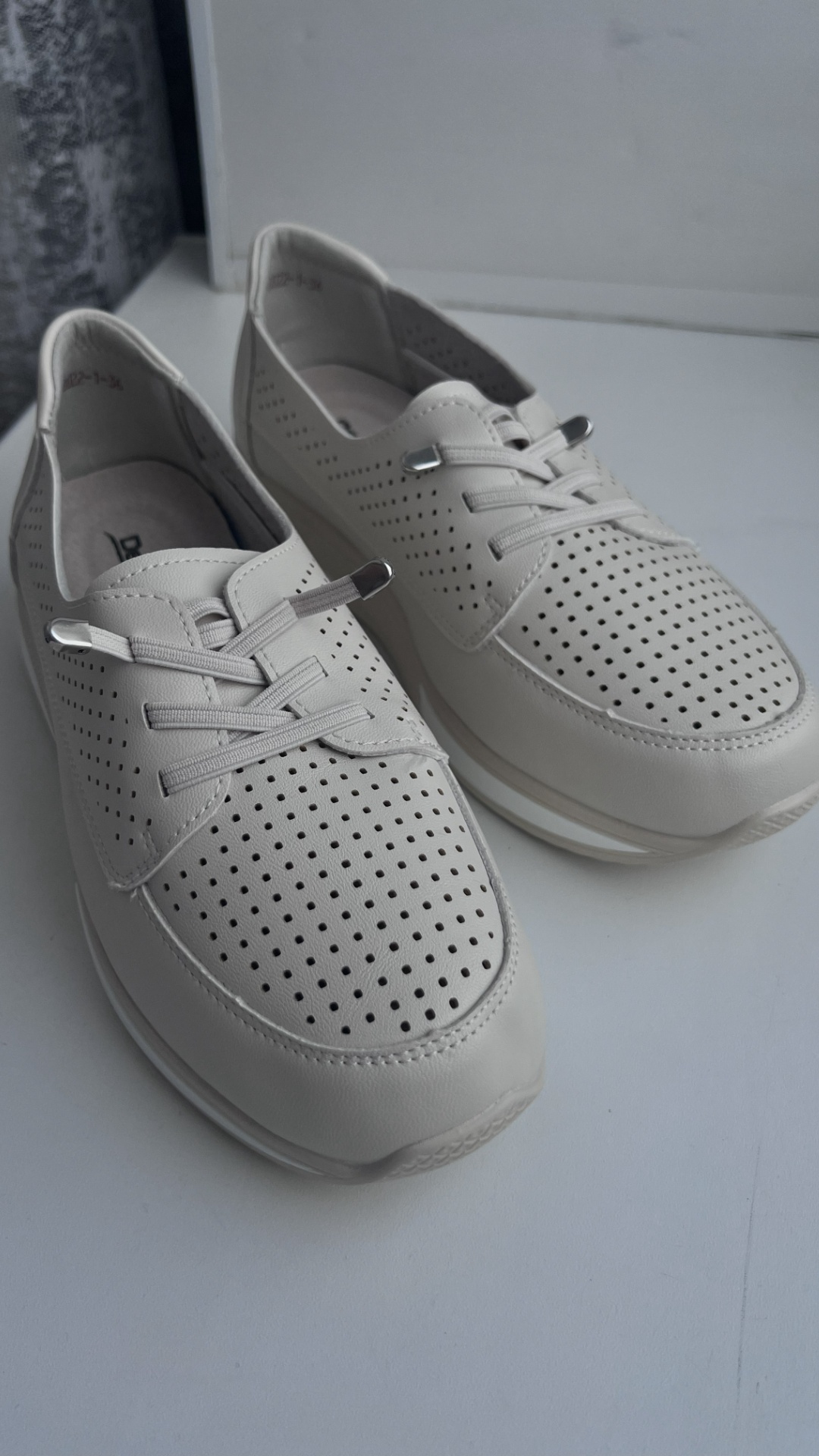 An ultra-realistic cinematic macro shot of light beige perforated leather casual sneakers. Soft, ...