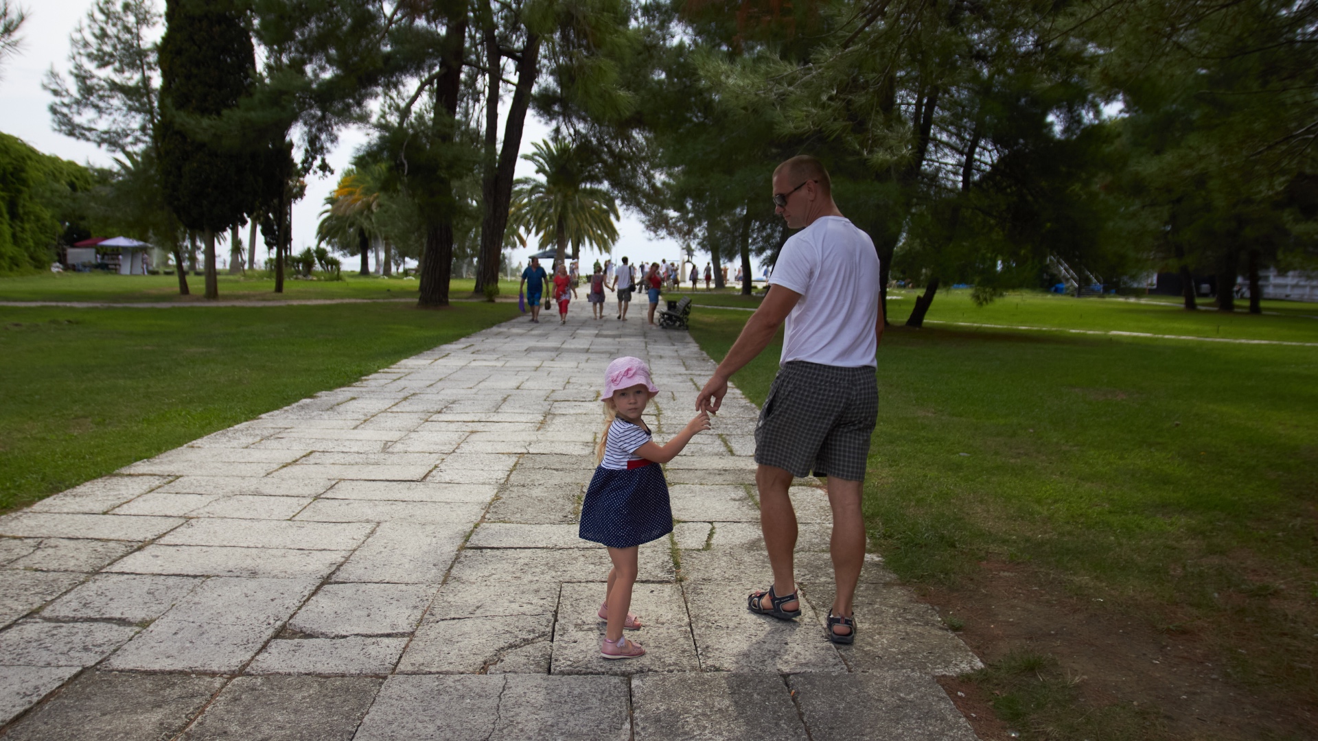 Father and daughter walking hand in hand. They both glance back at the camera, then the girl rele...