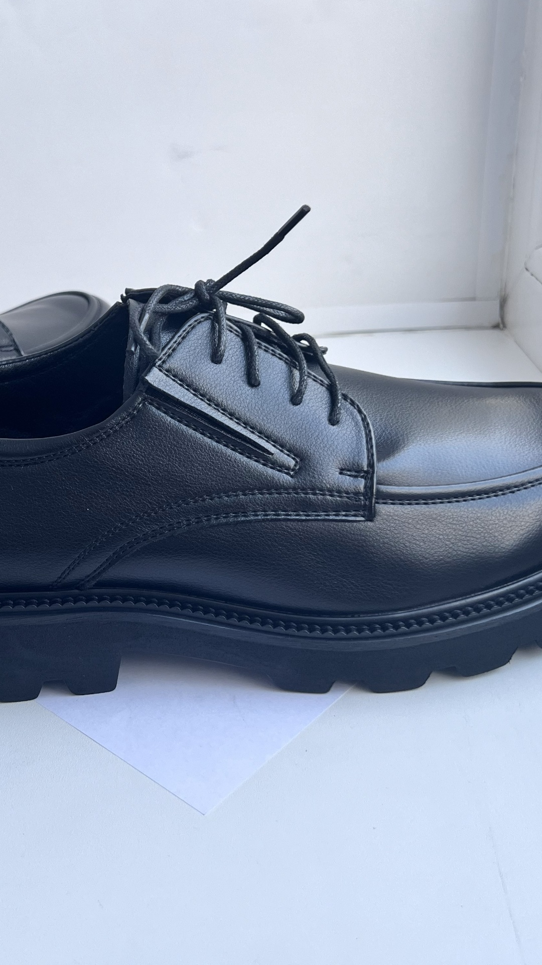 Extreme close-up of black laces being slowly tightened on a classic derby shoe. The fingers pull ...