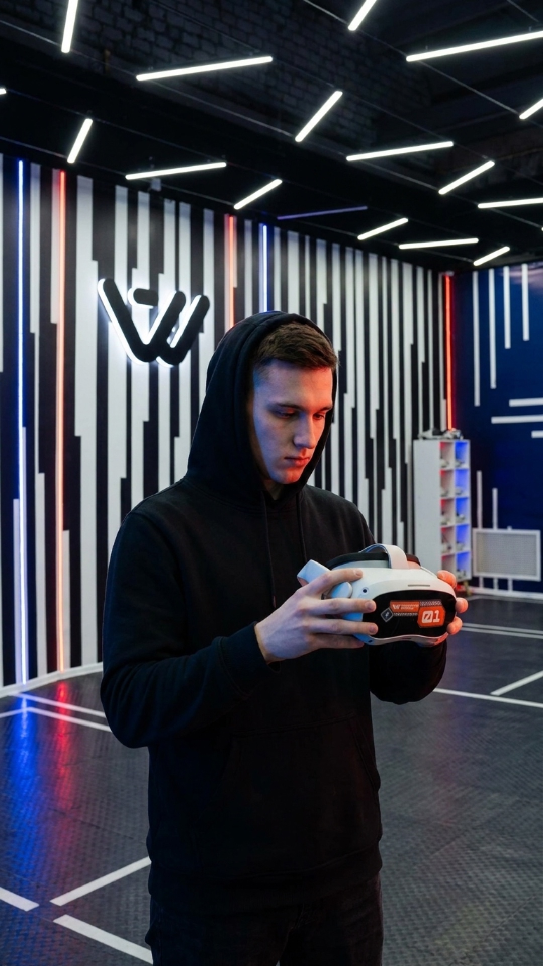 A young man is standing in a VR room with black and white vertical striped walls and neon lights....