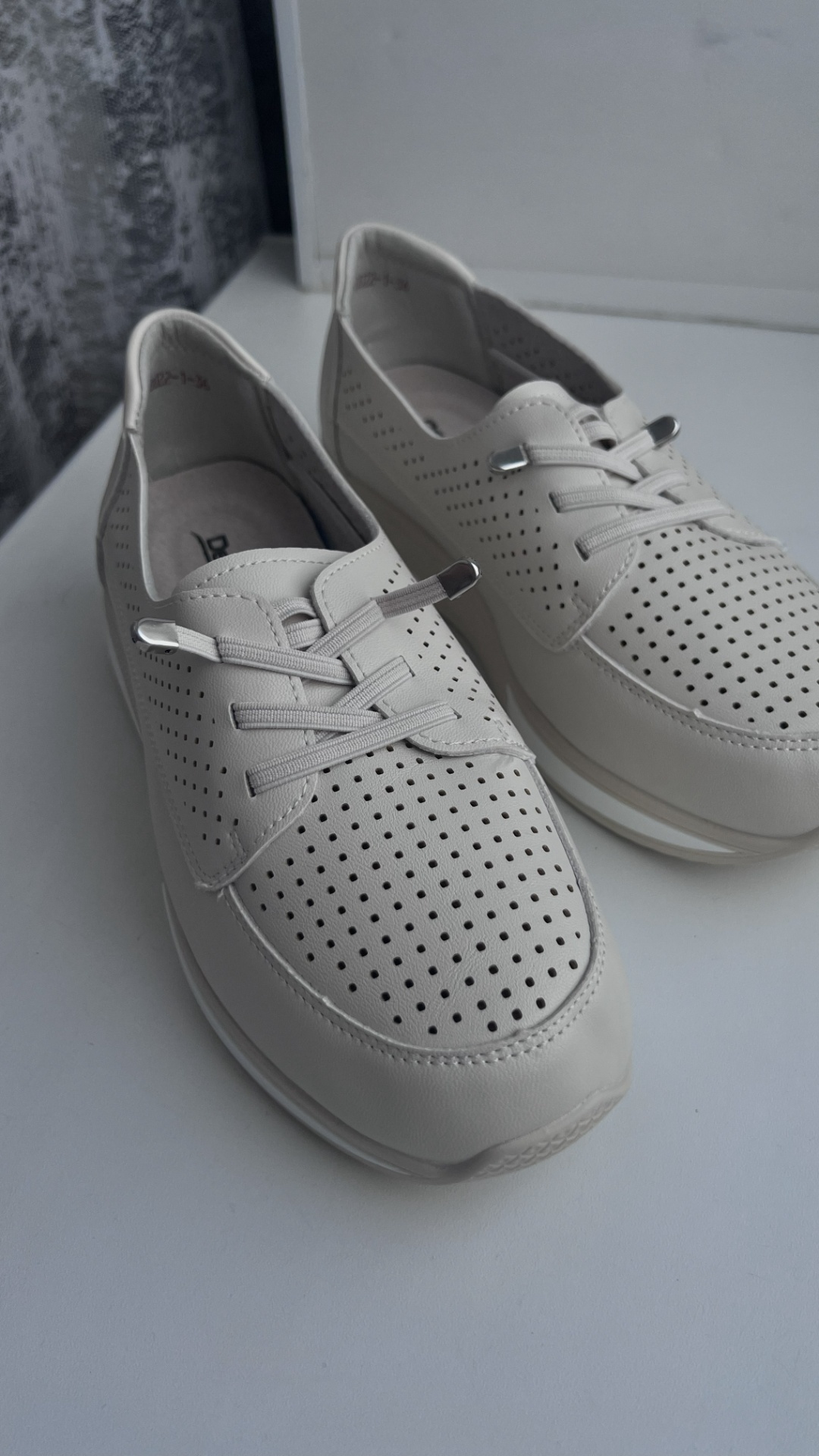 An ultra-realistic cinematic macro shot of light beige perforated leather sneakers. Soft, natural...