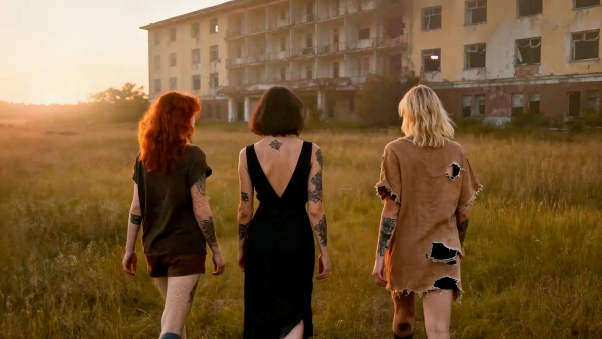 Les trois jeunes femmes avancent dans le terrain vague vers le bâtiment désaffecté.