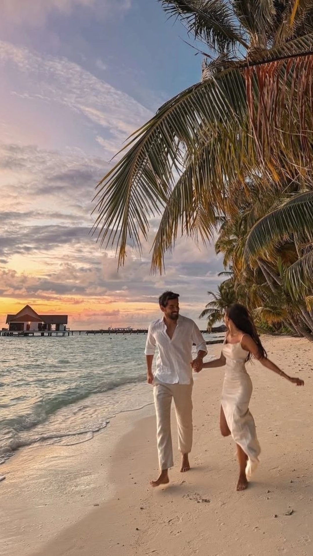Create a romantic and serene video inspired by the image of a couple walking hand-in-hand on a be...
