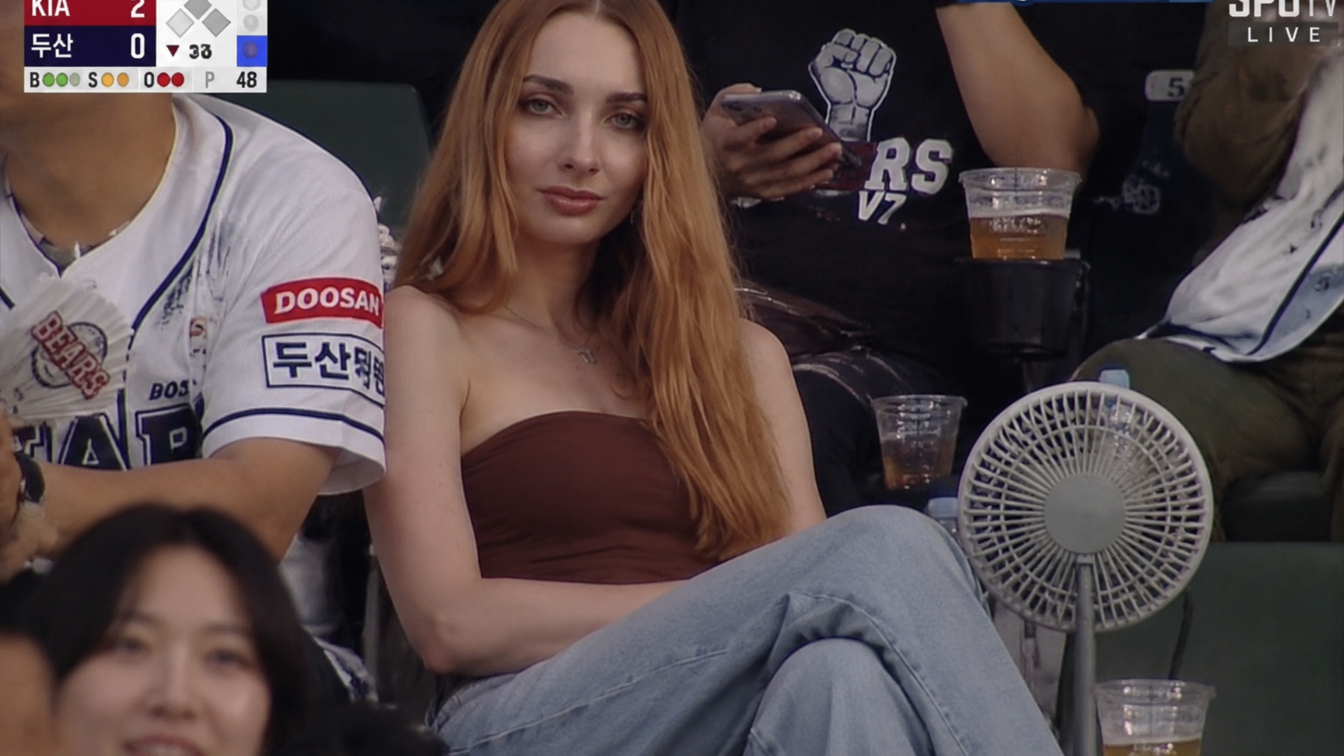 Realistic sports broadcast screenshot-style documentary video set in the spectator stands of a Ko...