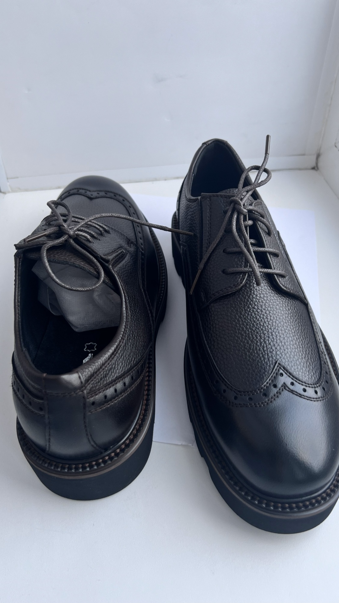 Extreme close-up cinematic shot of black grain leather brogue shoes with classic perforation (bro...