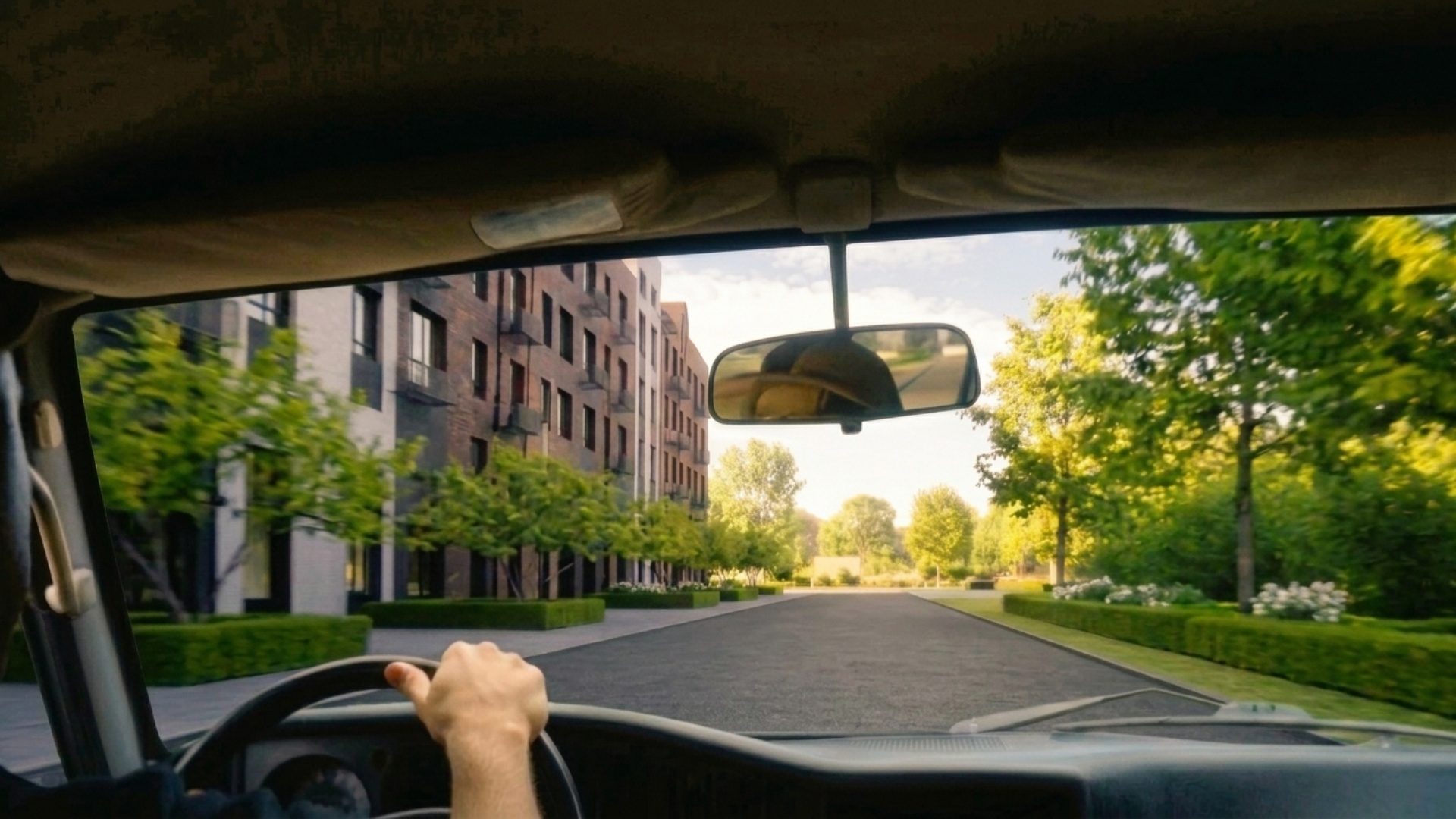 First-person POV from inside a car. The camera is positioned at driver eye level behind the steer...