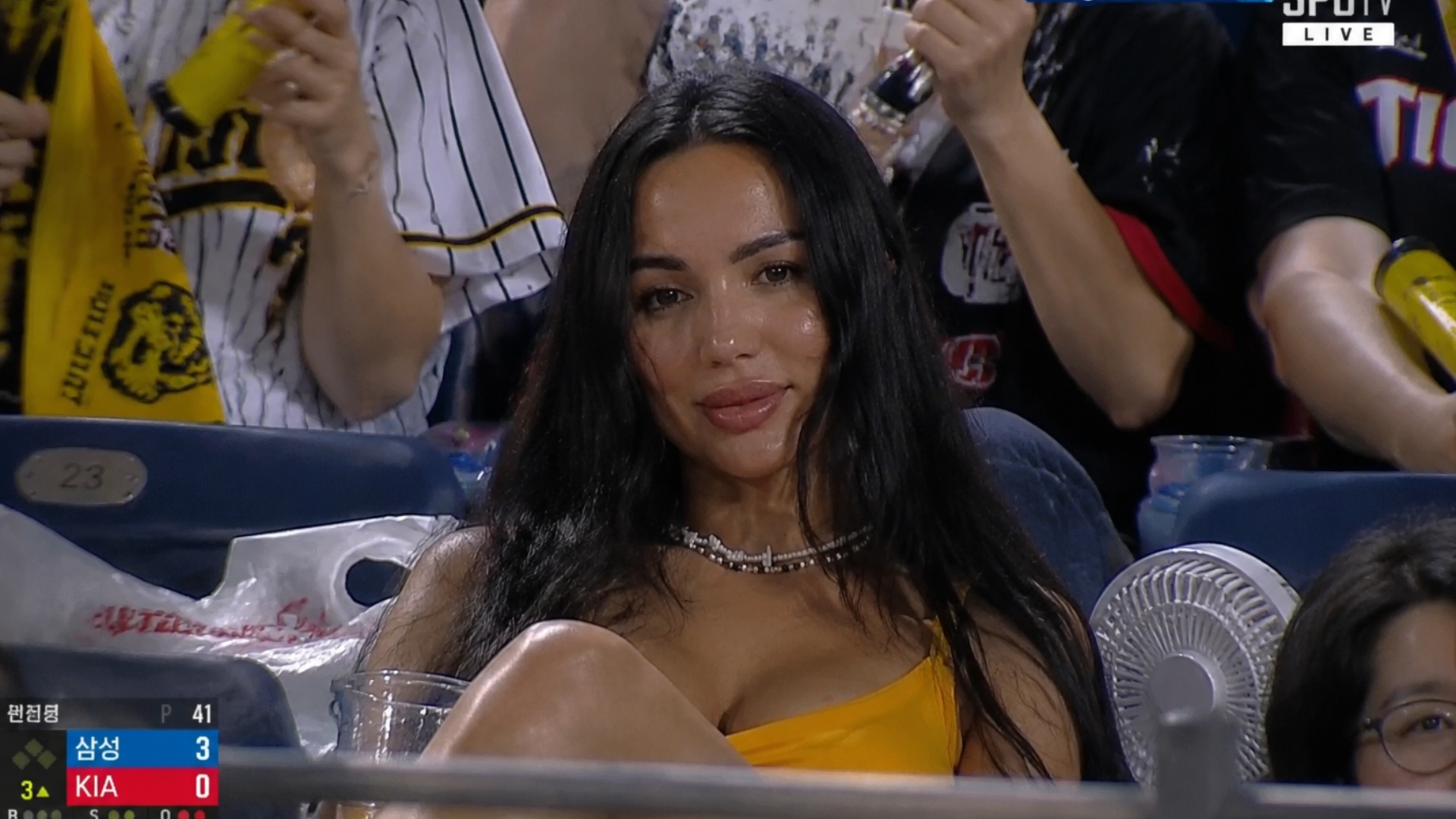 Realistic sports broadcast screenshot-style documentary video set in the spectator stands of a Ko...