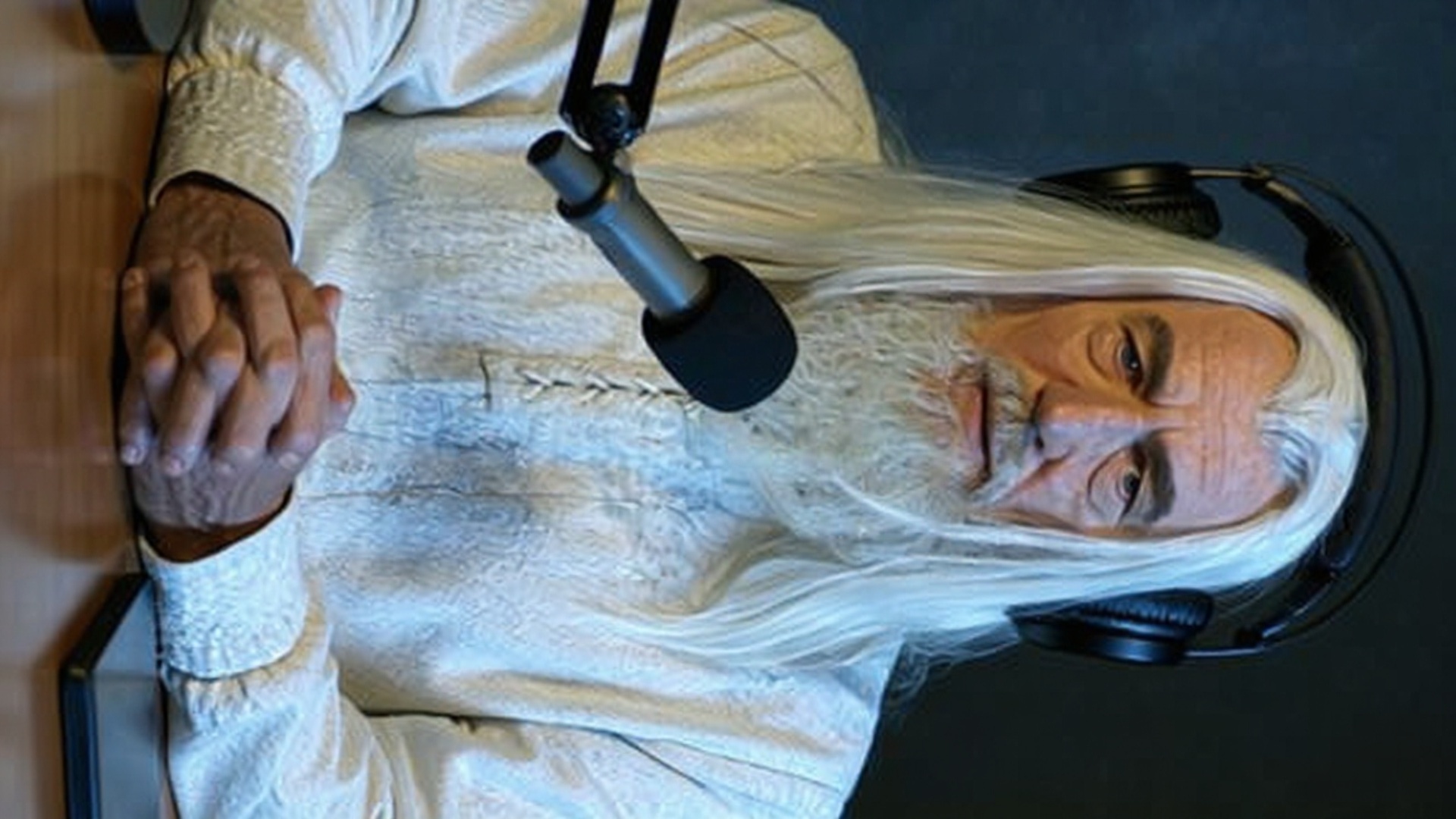 Animate this image so that the character is sitting at a podcast setup like on the Joe Rogan show...