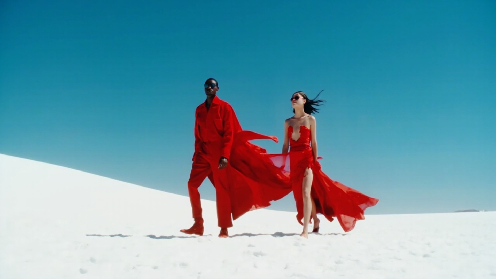 A high-fashion cinematic video scene in slow motion, set on a wide white desert with fine rippled...