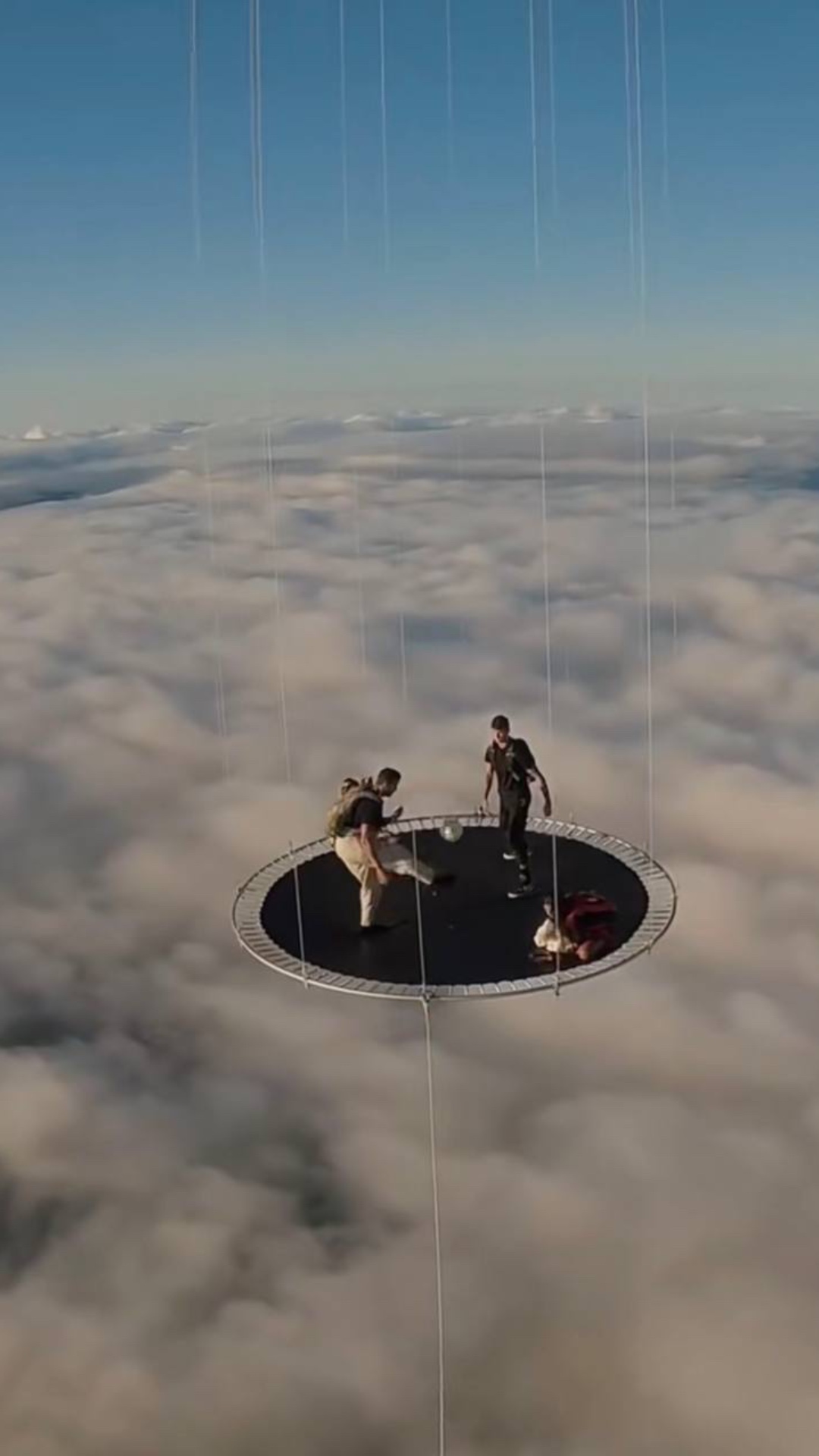 Cinematic wide shot of two athletic young men playing football on a giant trampoline floating hig...