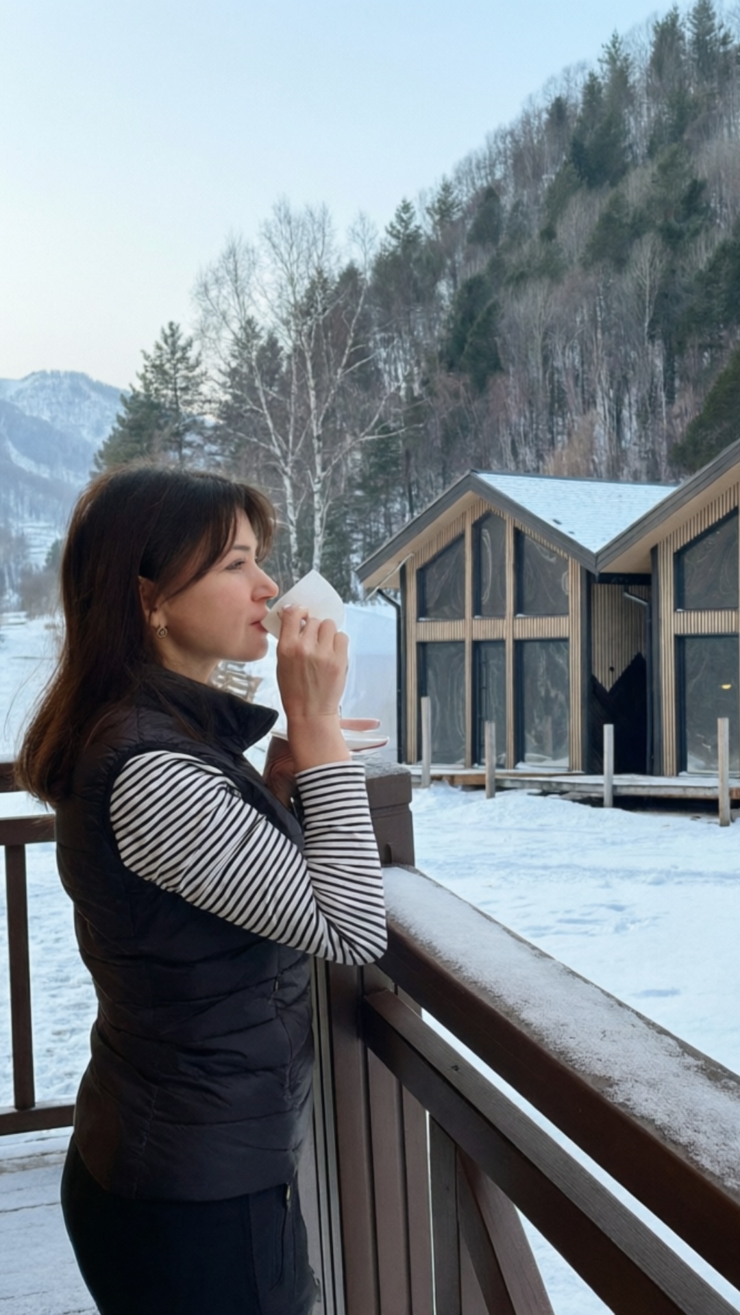 A girl on the veranda is drinking tea from a white mug, a little steam rising from the cup. She l...