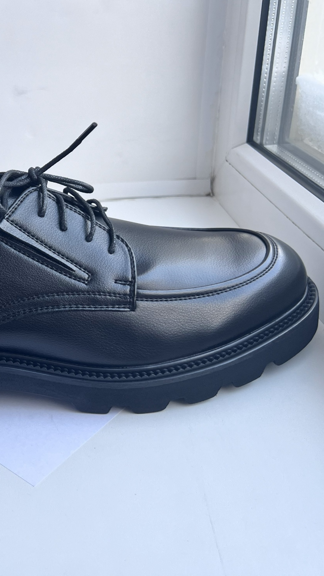 Macro close-up of fingers gently pressing into the side of a black leather derby shoe. The leathe...