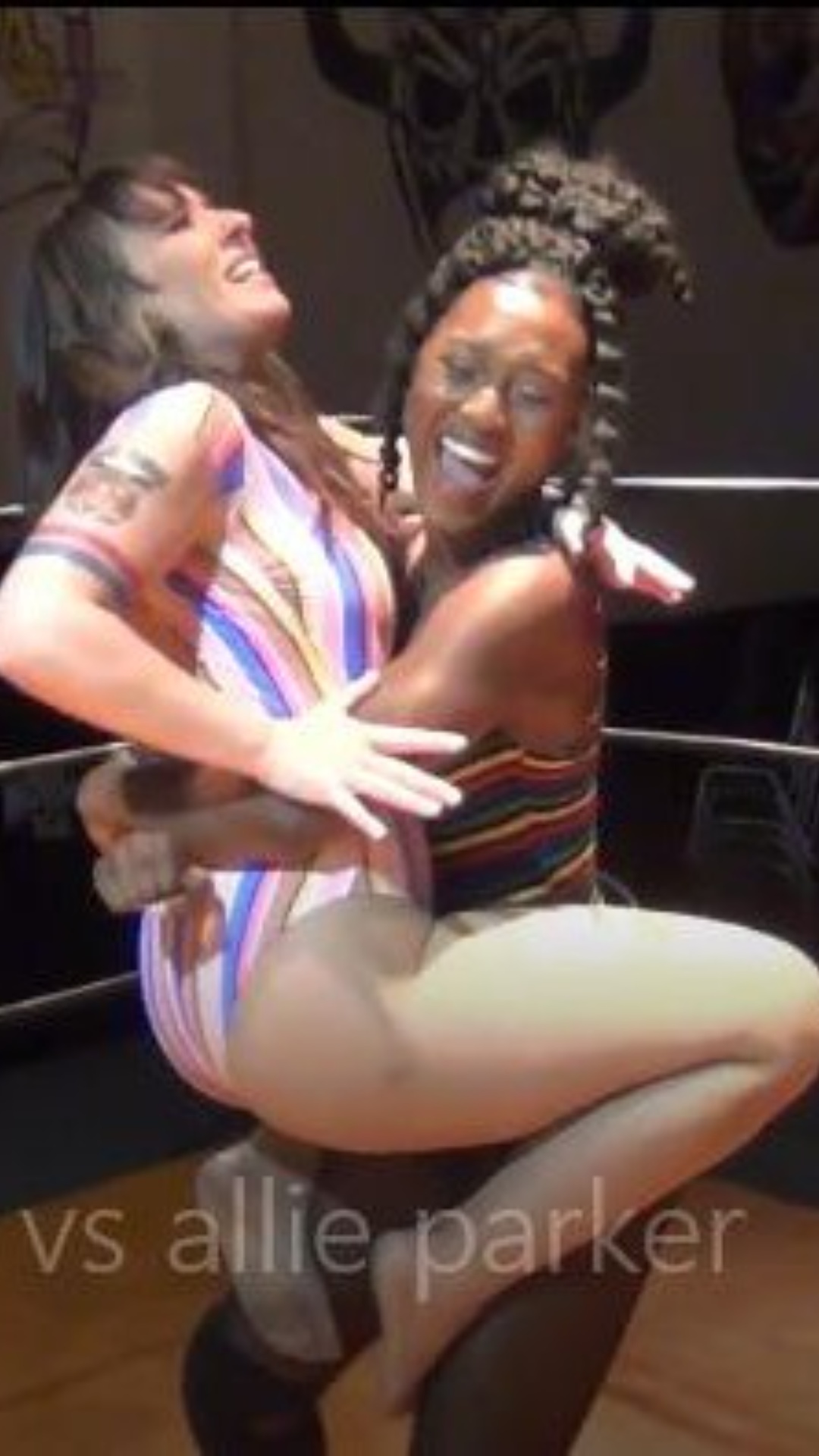 La negra, ejecuta una técnica de lucha libre conocida como bearhug sobre la joven de cabello cast...