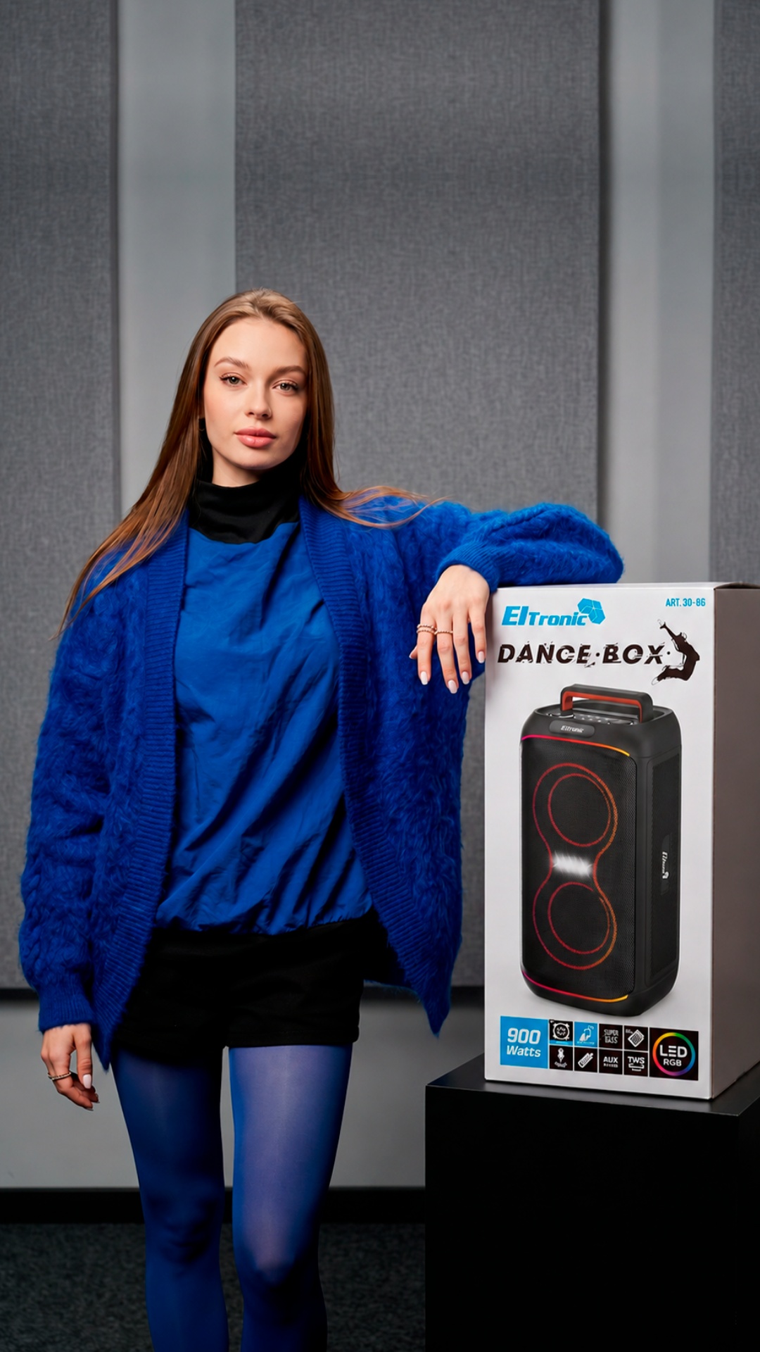 Static handheld commercial shot. A realistic young woman stands naturally beside a white Eltronic...